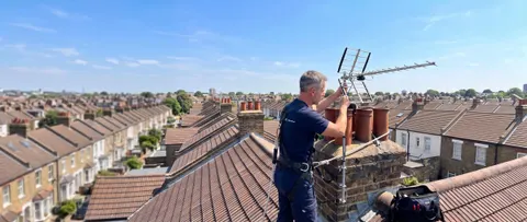 A SignalHub engineer in a safety harness adjusting a TV aerial on a chimney